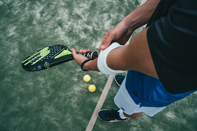 Tennisspieler hält einen Tennisschläger und zupft an seinem Schweißband - Maxiflug Tennisreisen